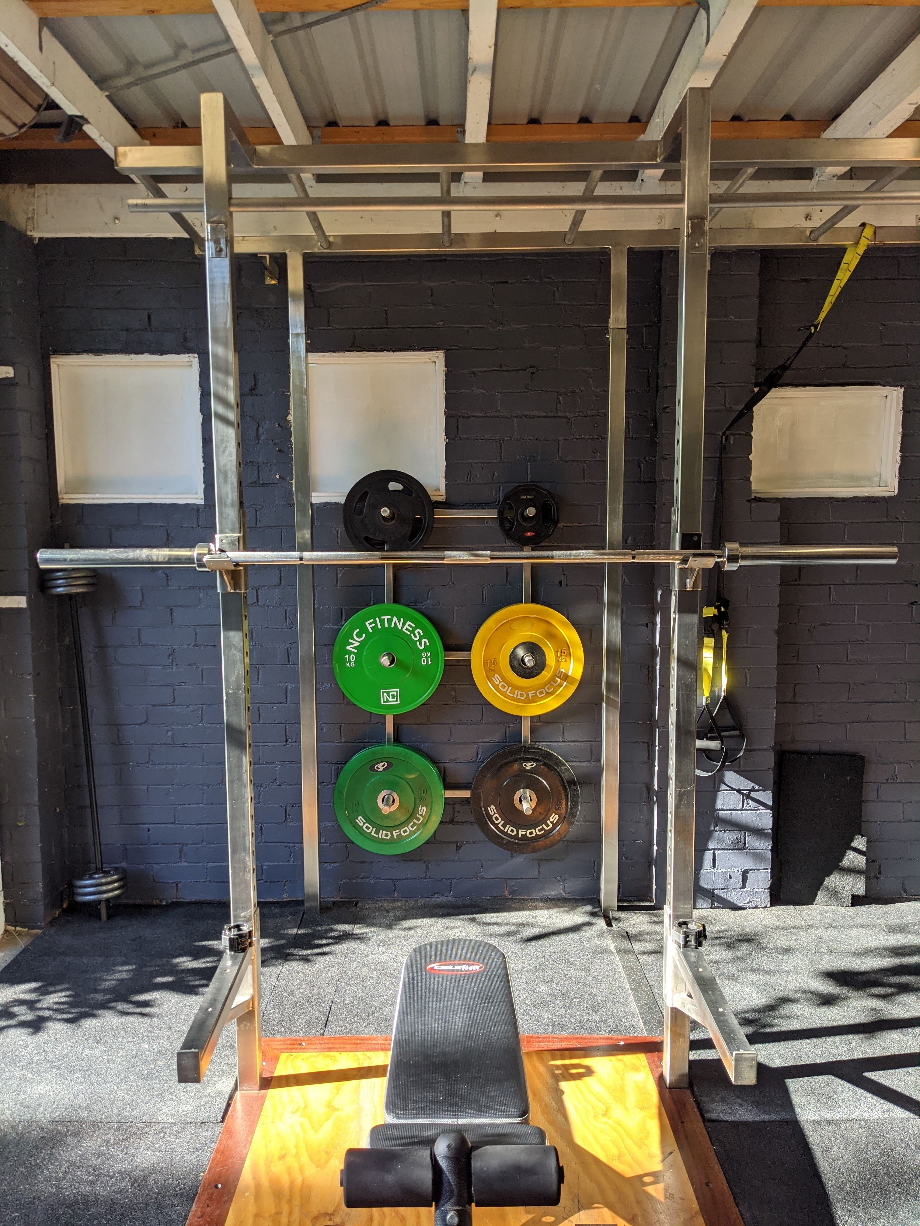 An empty steel training rack and bench in a sunlit gym.